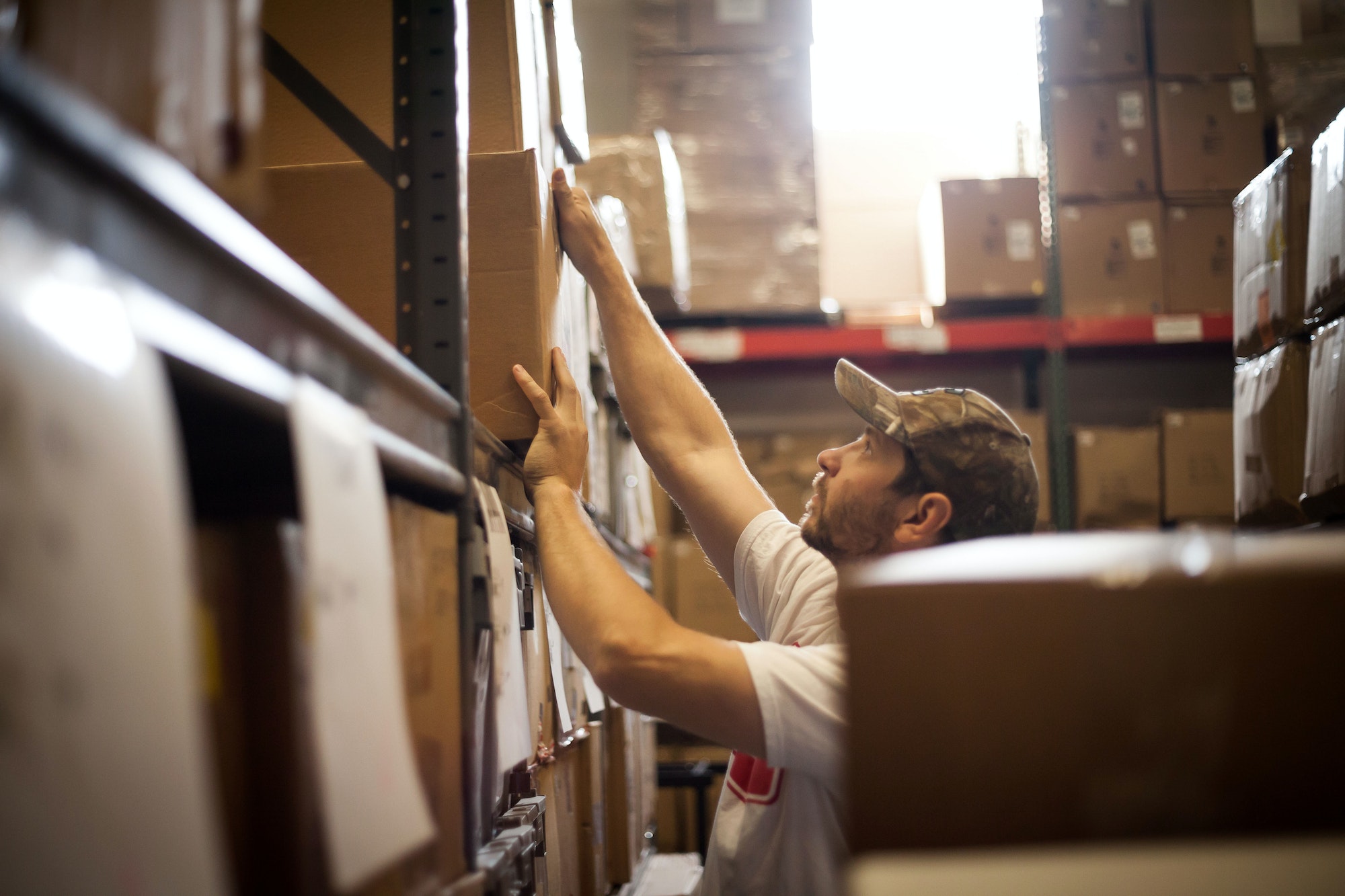 Worker reaching up for cardboard box stored in warehouse